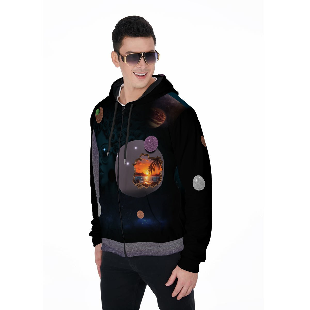 A man wearing a black zip-up hoodie with a complex cosmic and tropical sunset graphic print, styled with dark sunglasses and black pants against a plain white background.